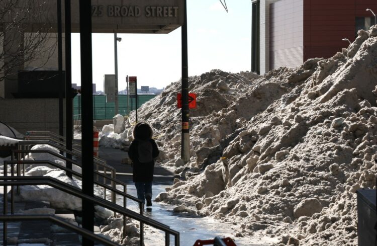 A person walks by as New York City Department of Sanitation scoop up snow to uses one of its eight massive "hot tubs" in Lower Manhattan January 30, 2026 can melt up to 120 tons of snow per hour. The snow is lifted and dumped into the massive hot tubs and spewed into the sewers as water. Snow pushed to the curb and the roadside isnt melting naturally, complicating pedestrians journeys and leaving some cars immobilized. With weather expected to remain frigid for at least a couple of weeks, if we dont melt it, itll be there for a while, explained New York Sanitation Department official Javier Lojan at a press conference on January 28, 2026. (Photo by TIMOTHY A. CLARY / AFP)