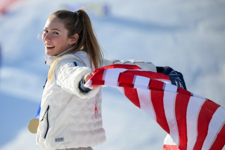 USA's gold medalist Mikaela Shiffrin celebrates with her national flag during the podium ceremony of the women's slalom event during the Milano Cortina 2026 Winter Olympic Games at the Tofane Alpine Skiing Centre in Cortina dAmpezzo on February 18, 2026. (Photo by Marco BERTORELLO / AFP)
